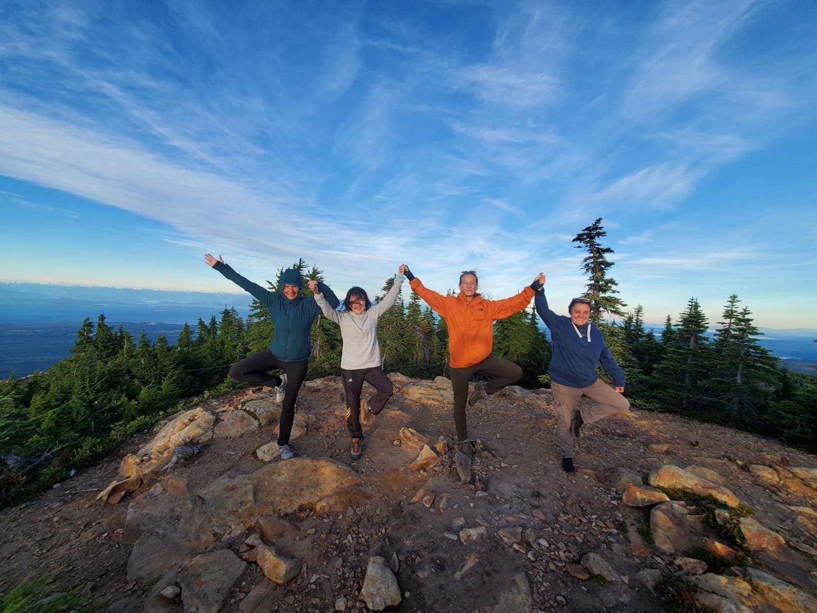 Four friends with arms raised on a BC mountain summit at sunset