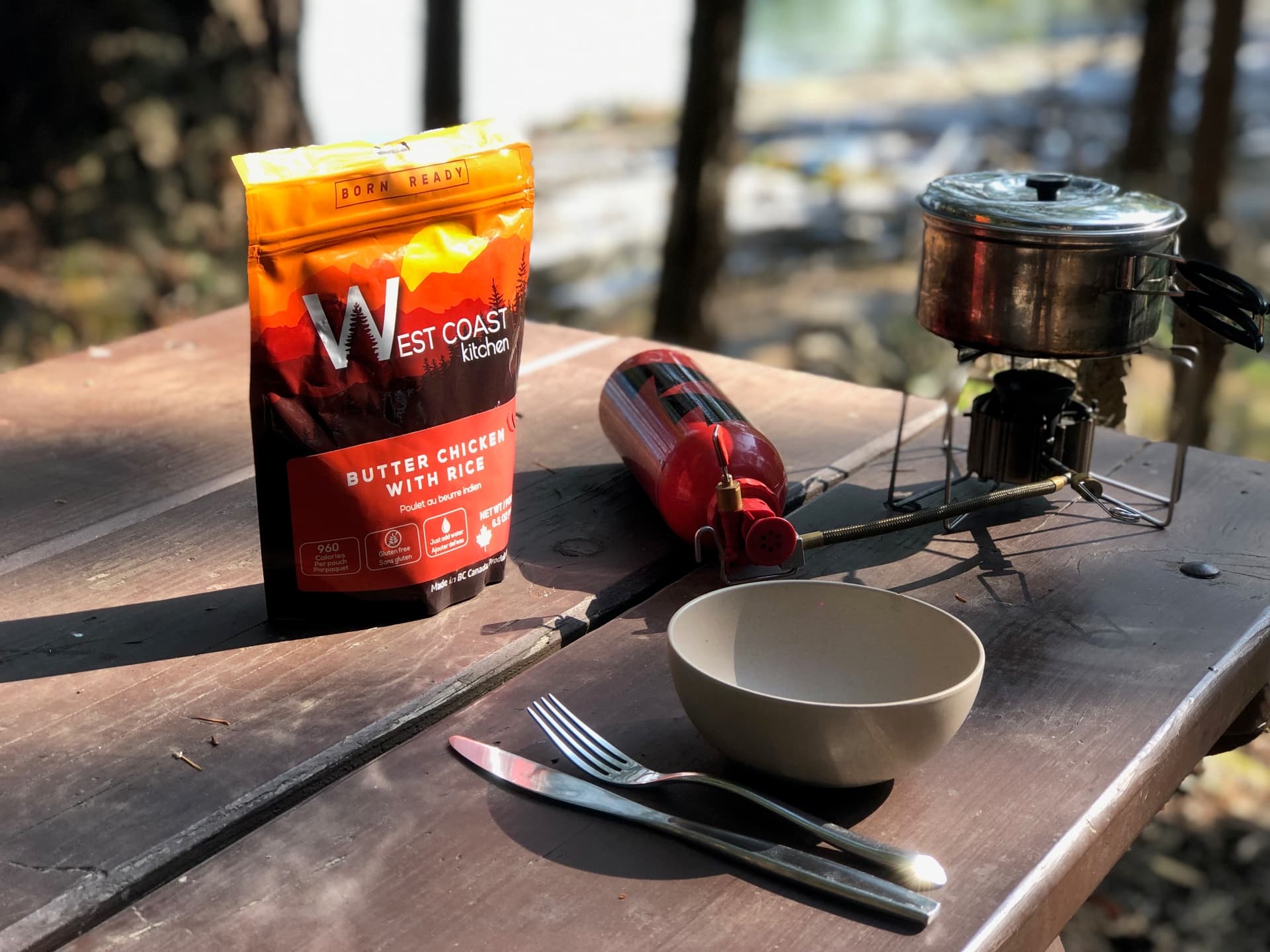 WCK Butter Chicken with Rice pouch on a wooden picnic table beside a camp stove