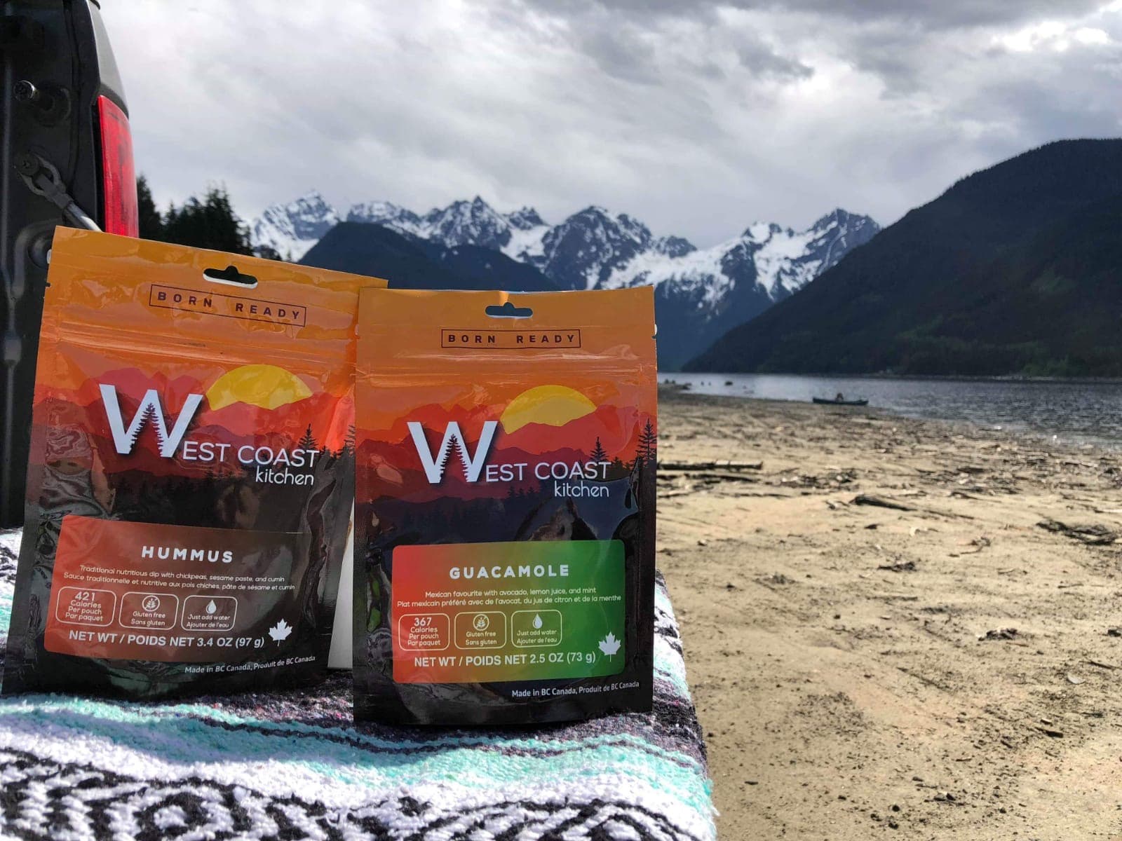 WCK Hummus and Guacamole pouches on a beach blanket with snowy mountains and lake behind